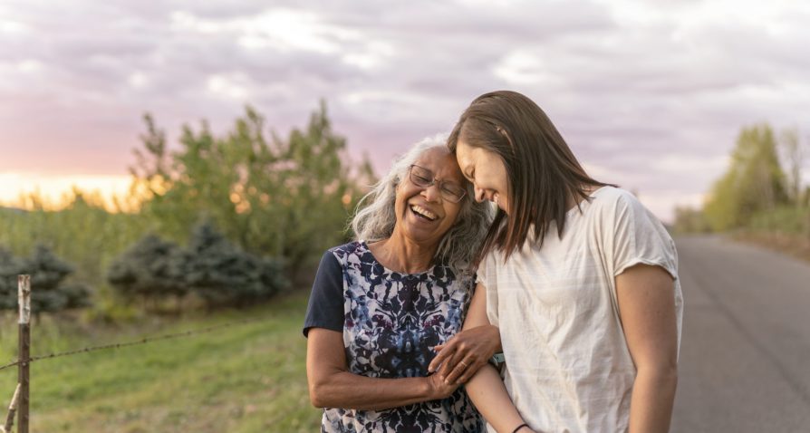 A beautiful senior mom of pacific island descent is walking outdoors with her adult thirty something year old daughter. They are enjoying each others company and soaking in the gorgeous, colorful, sunset.