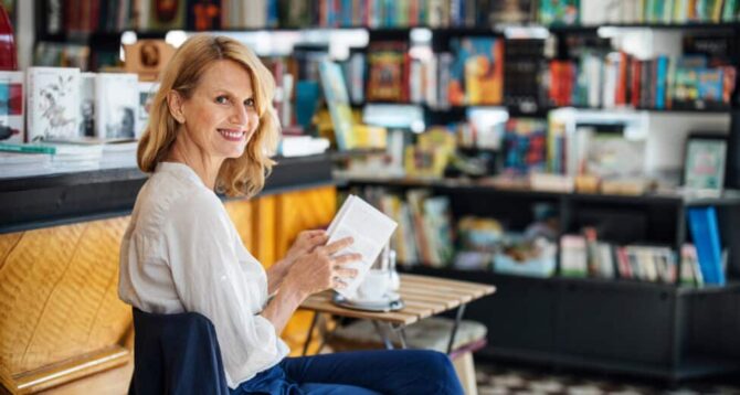 Smiling mature woman sitting in a bookstore cafe with a book. Happy female customer in a bookstore reading a book.